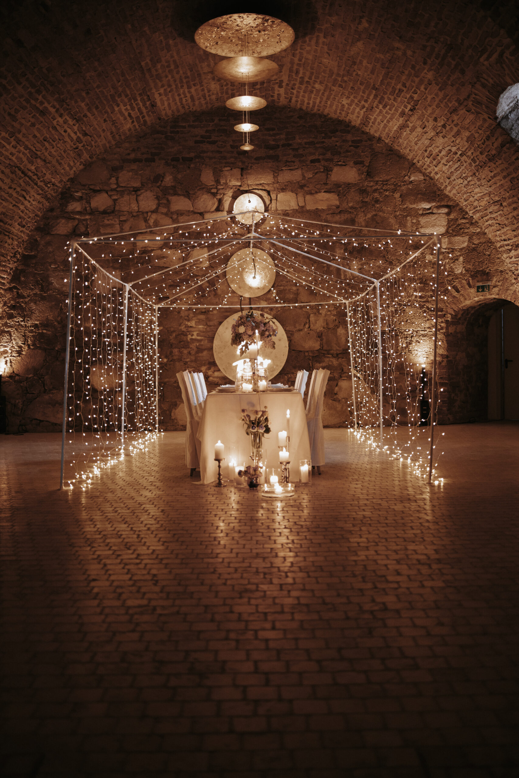 Romantische Hochzeitslocation mit gedecktem Tisch und glitzernd leuchtendem Lichterkettenbaldachin